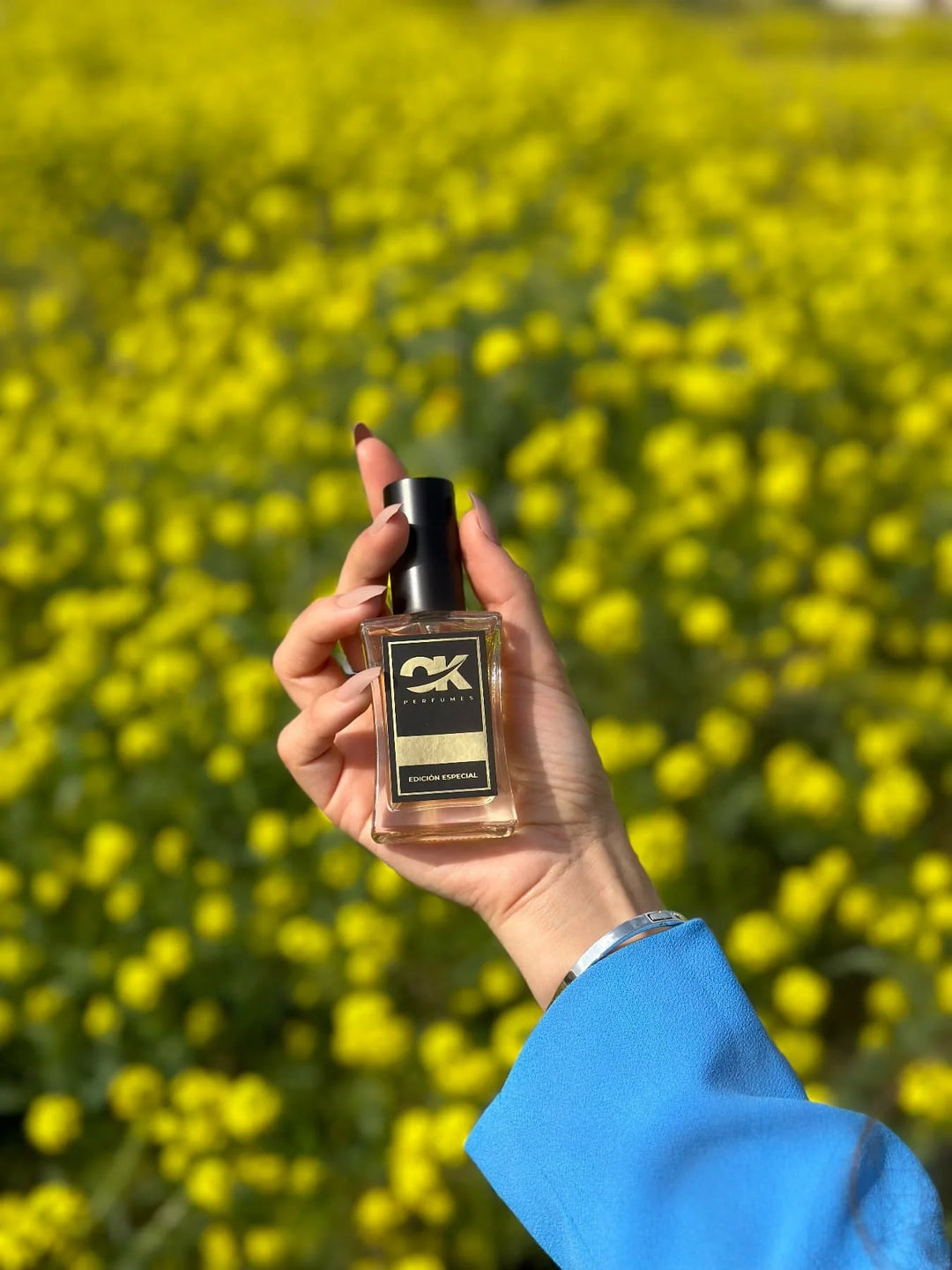 Una persona sostiene un Pack Nicho de OK Perfumes frente a un campo de flores. (calidad)